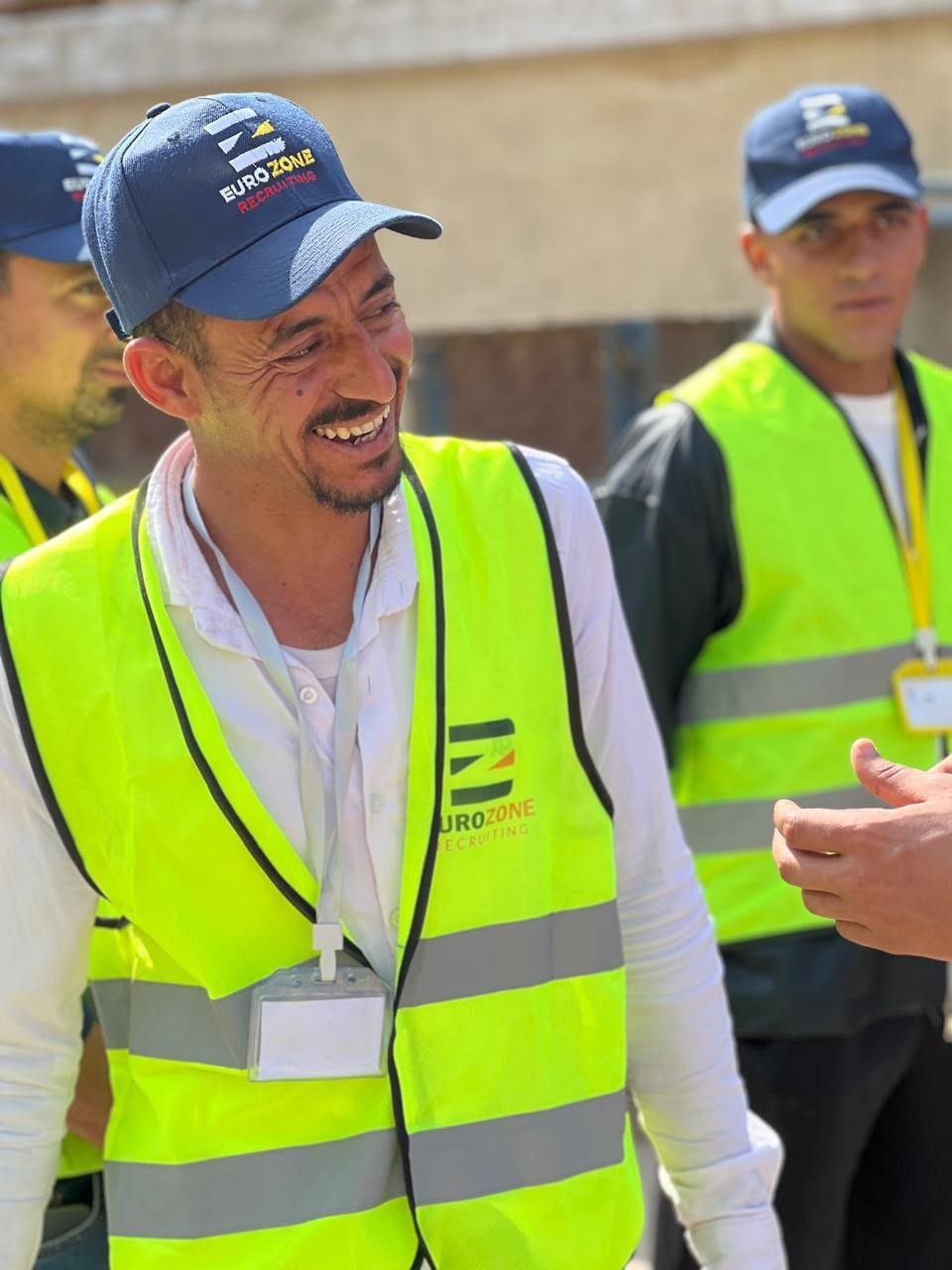 A Eurozone worker smiling in the company's hi-vis vest and cap, with two more of the crew in the same vests behind him.