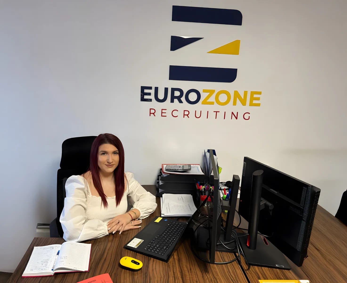 A colleague at their desk, under the Eurozone Recruiting sign on the office wall.