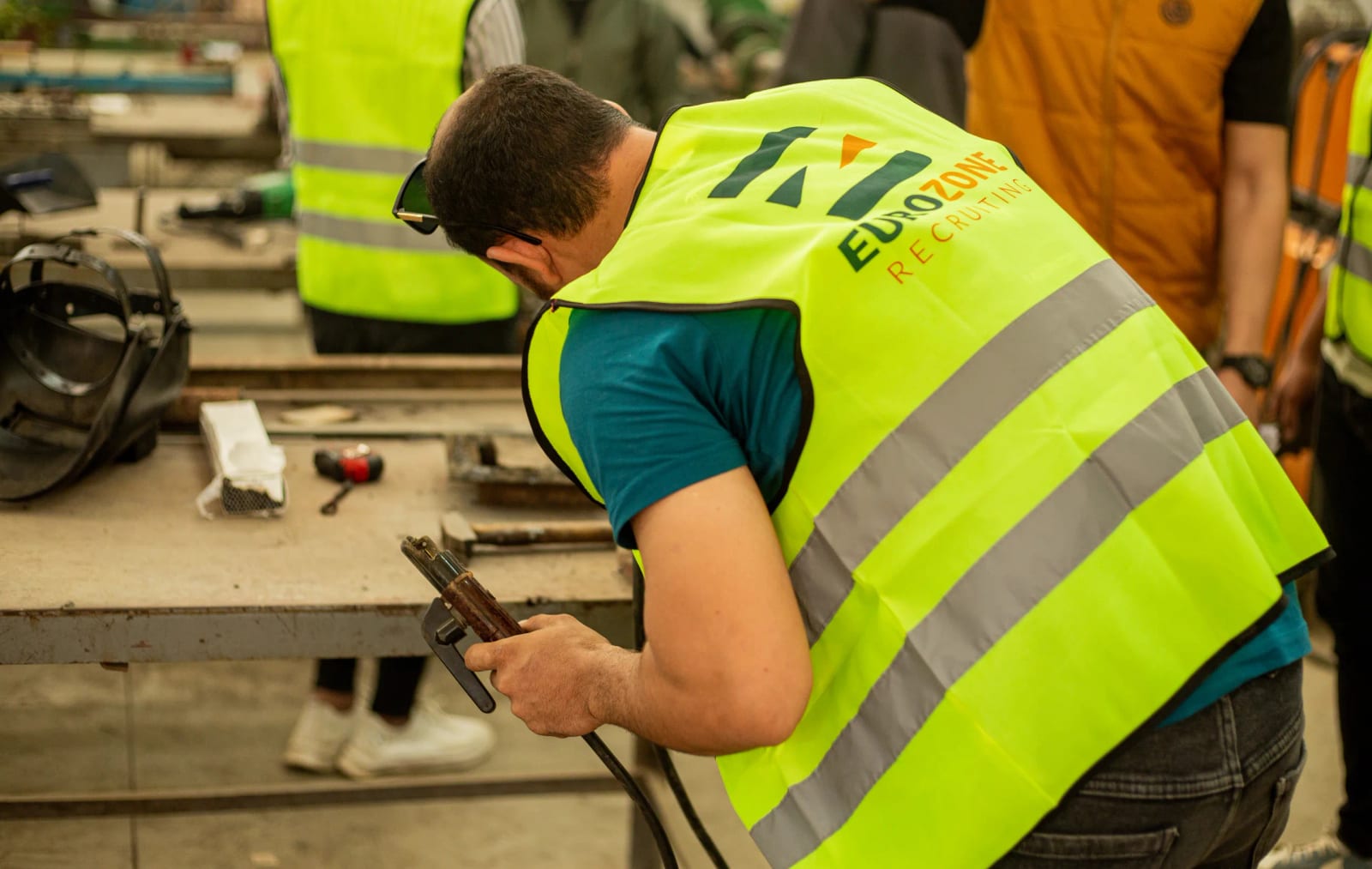 A Eurozone worker smiling in the company's hi-vis vest and cap, with two more of the crew in the same vests behind him.