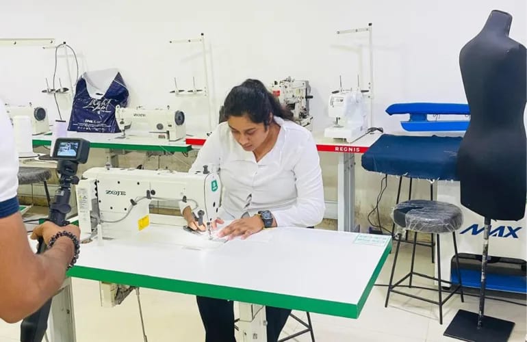 Someone sewing at an industrial machine in a tailoring workshop while a camera films the work trial.